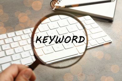 Woman looking at word Keyword and keyboard through magnifying glass, closeup