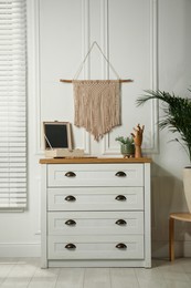 Photo of Cozy room interior with chest of drawers and stylish macrame on wall