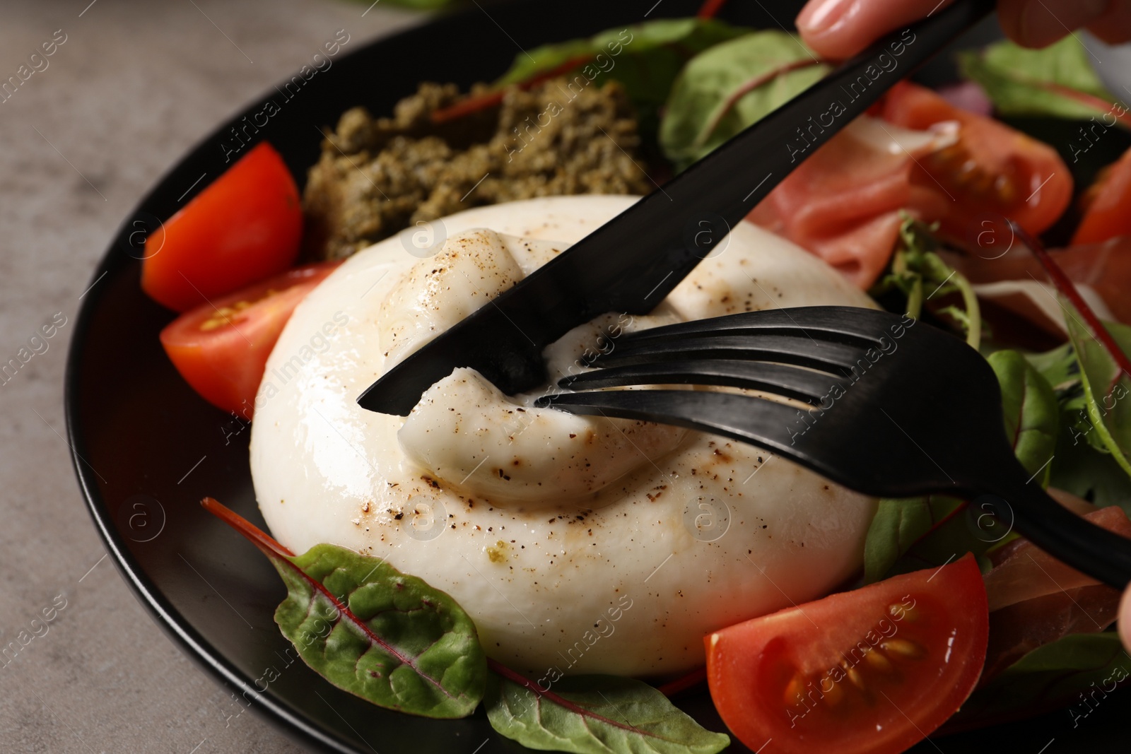 Photo of Woman eating delicious burrata salad at grey table, closeup