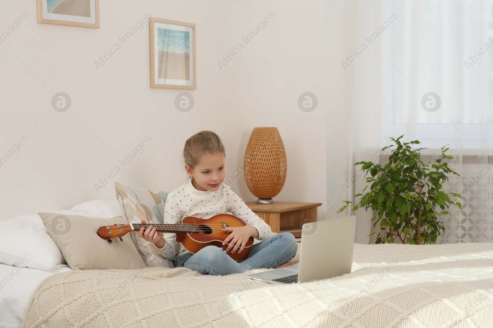 Photo of Little girl learning to play ukulele with online music course at home. Space for text