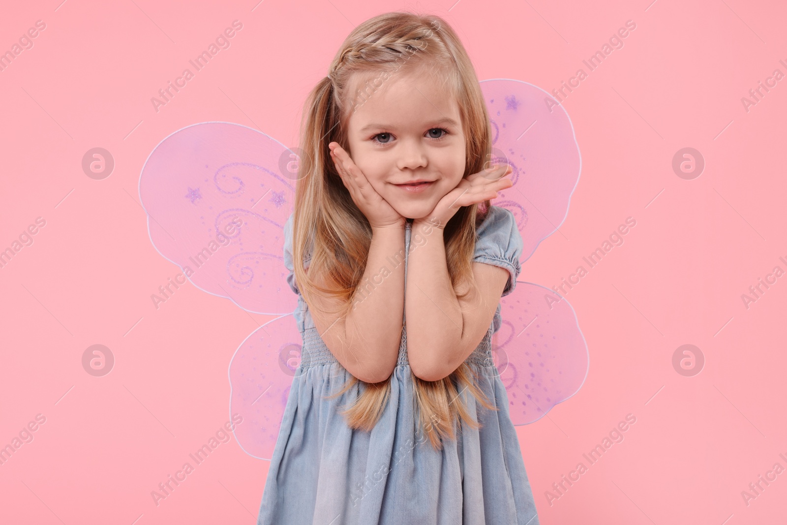 Photo of Cute little girl in fairy costume with violet wings on pink background