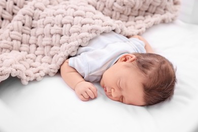 Cute newborn baby sleeping under beige soft blanket on bed