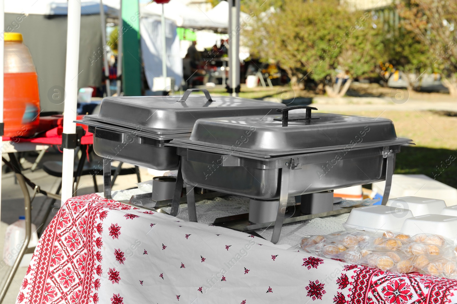 Photo of Volunteer food distribution. Metal warmers with delicious dishes on table outdoors.