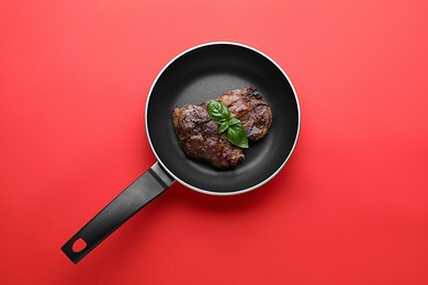 Photo of Tasty fried steak in pan on red background, top view