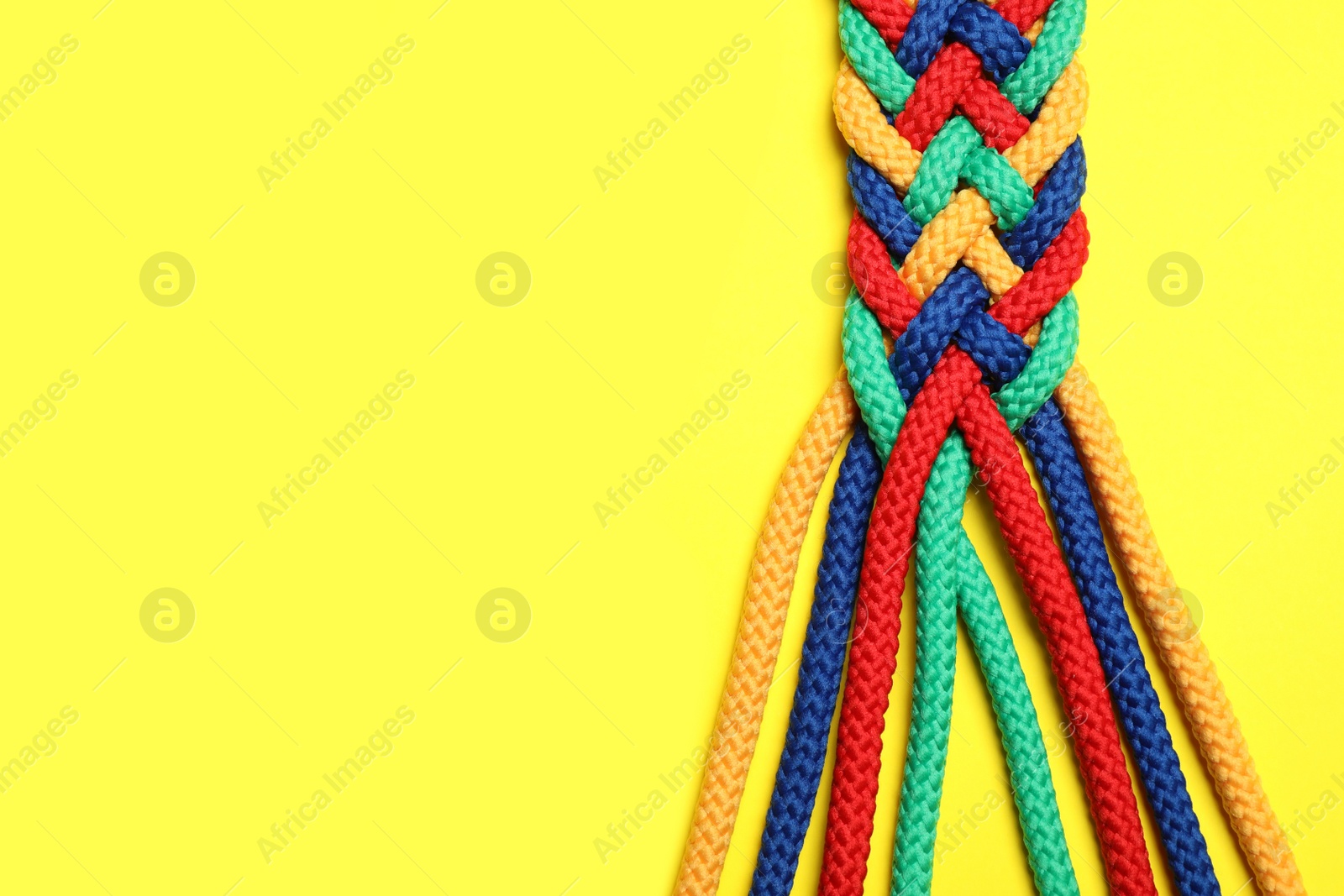 Photo of Top view of braided colorful ropes on yellow background, space for text. Unity concept