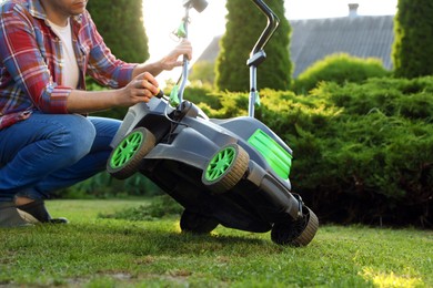 Photo of Man with screwdriver fixing lawn mower in garden, closeup