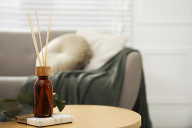 Reed diffuser with eucalyptus on wooden table in living room. Space for text