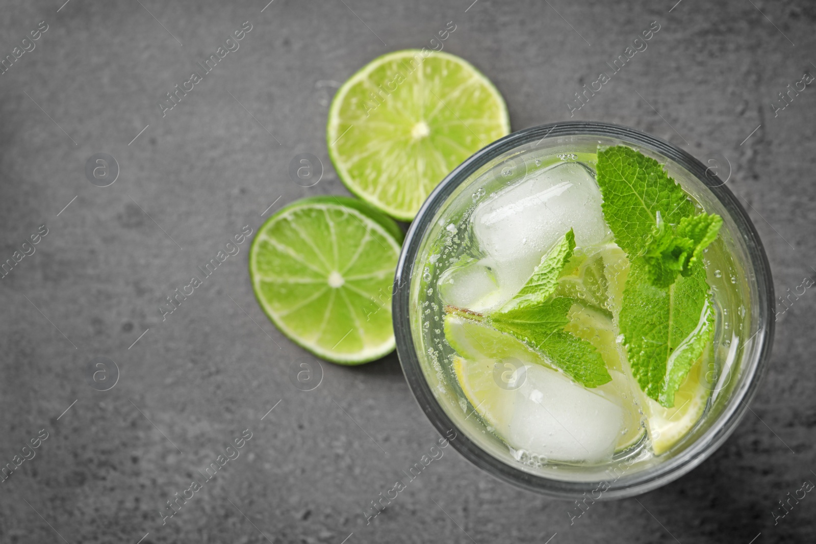 Photo of Refreshing beverage with mint and lime in glass on grey background, top view