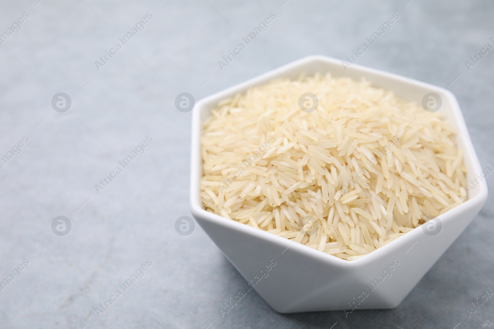 Photo of Raw rice in bowl on light grey table, closeup. Space for text
