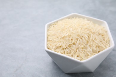 Raw rice in bowl on light grey table, closeup. Space for text