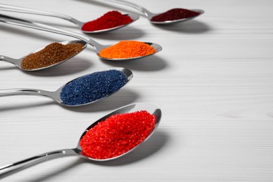 Spoons with different food coloring on white wooden table, closeup. Space for text