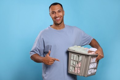 Photo of Happy man with basket full of laundry on light blue background
