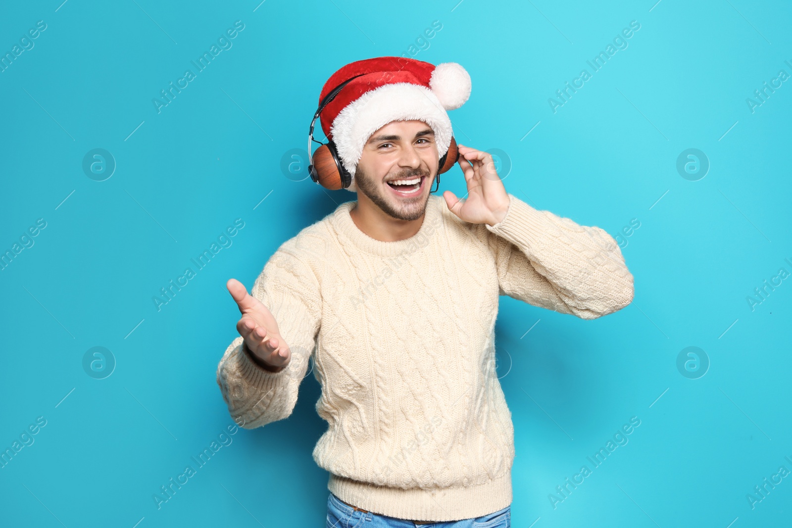 Photo of Young man in Santa hat listening to Christmas music on color background