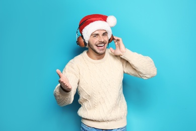 Young man in Santa hat listening to Christmas music on color background