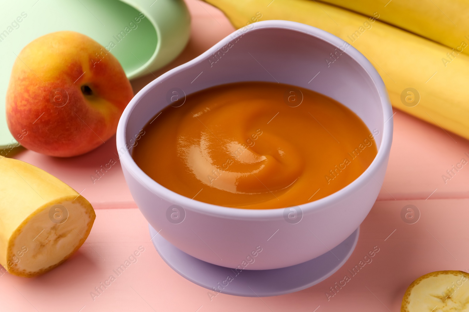 Photo of Healthy baby food in bowl and fresh fruits on pink wooden table, closeup
