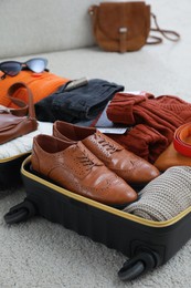 Open suitcase with folded clothes, accessories and shoes on floor indoors, closeup