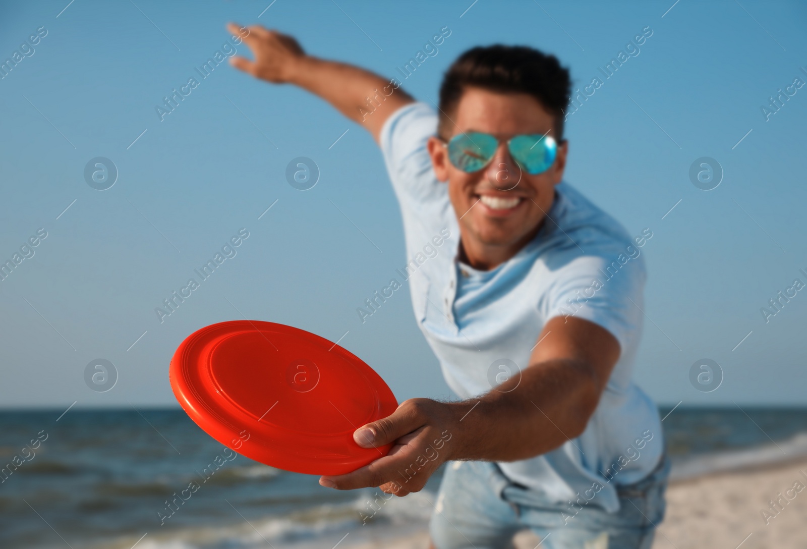 Photo of Happy man throwing flying disk at beach, focus on hand