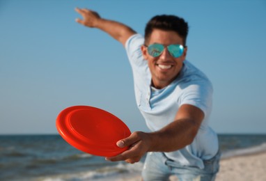 Photo of Happy man throwing flying disk at beach, focus on hand