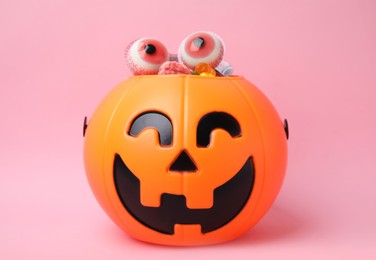 Photo of Halloween trick or treat bucket with different sweets on pink background