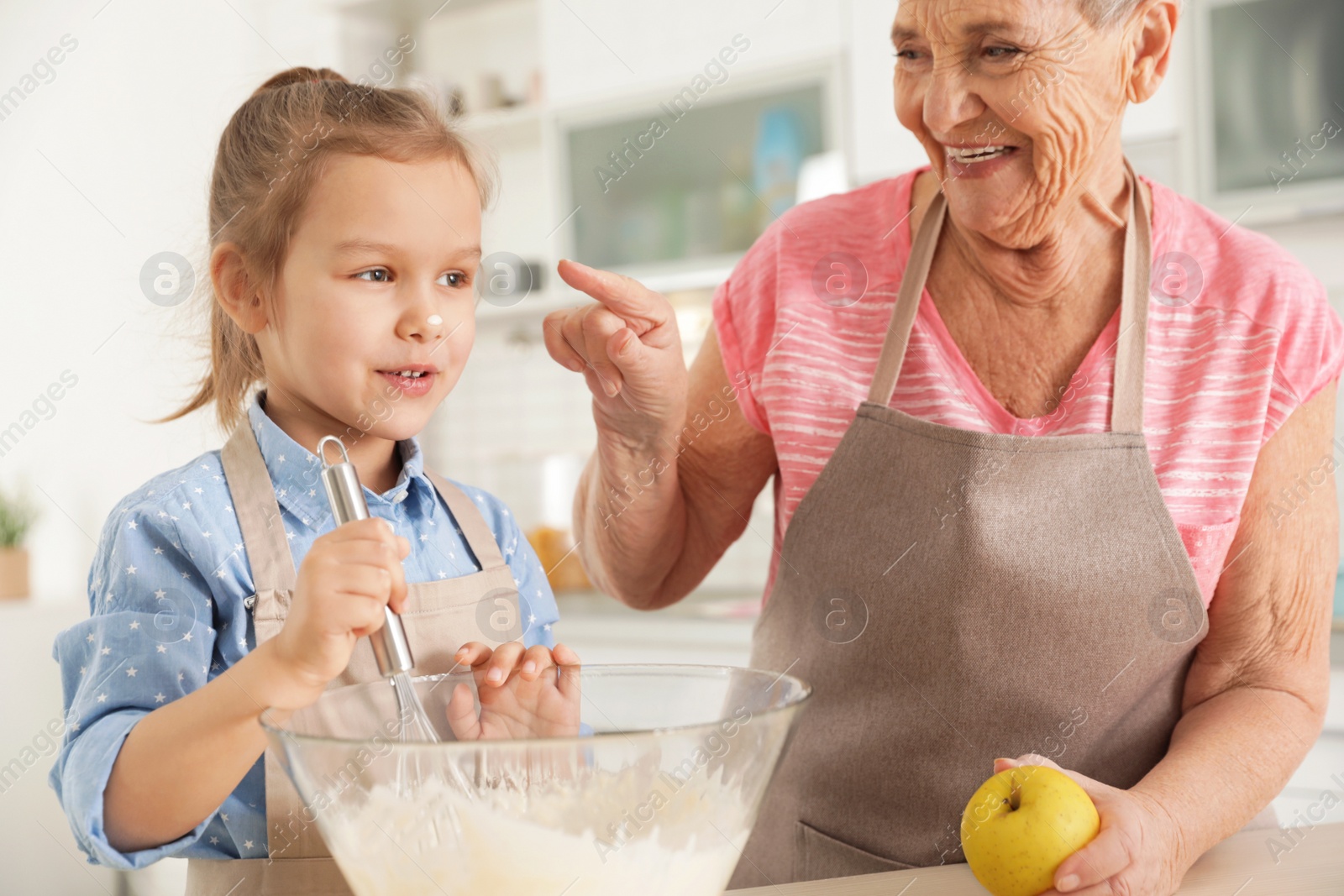 Photo of Cute girl and her grandmother cooking in kitchen