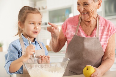 Cute girl and her grandmother cooking in kitchen