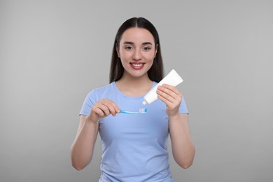 Photo of Happy woman squeezing toothpaste from tube onto plastic toothbrush on light grey background