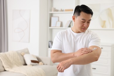 Photo of Handsome man applying body cream onto his arm indoors. Space for text