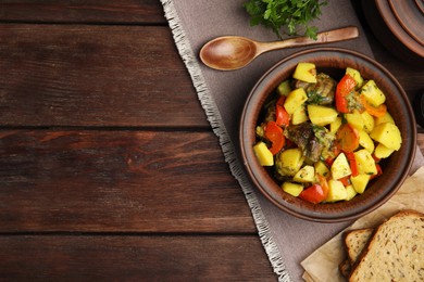 Photo of Tasty cooked dish with potatoes in earthenware served on wooden table, flat lay. Space for text