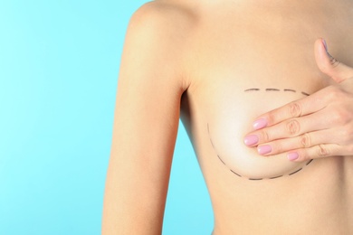 Photo of Young woman with marks on breast for cosmetic surgery operation against color background, closeup