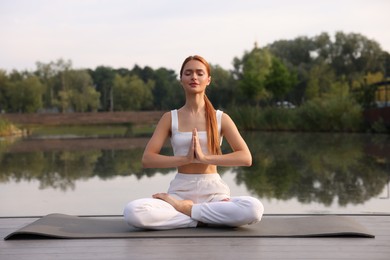 Photo of Beautiful young woman practicing Padmasana on yoga mat outdoors. Lotus pose