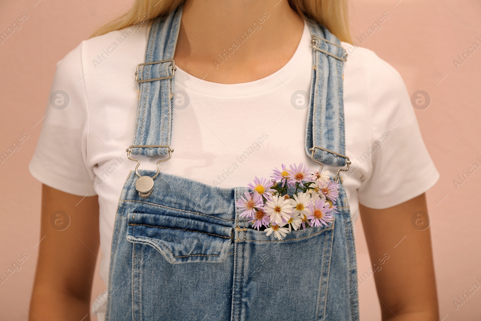 Photo of Woman with beautiful tender flowers in denim jumpsuit's pocket on pale orange background, closeup