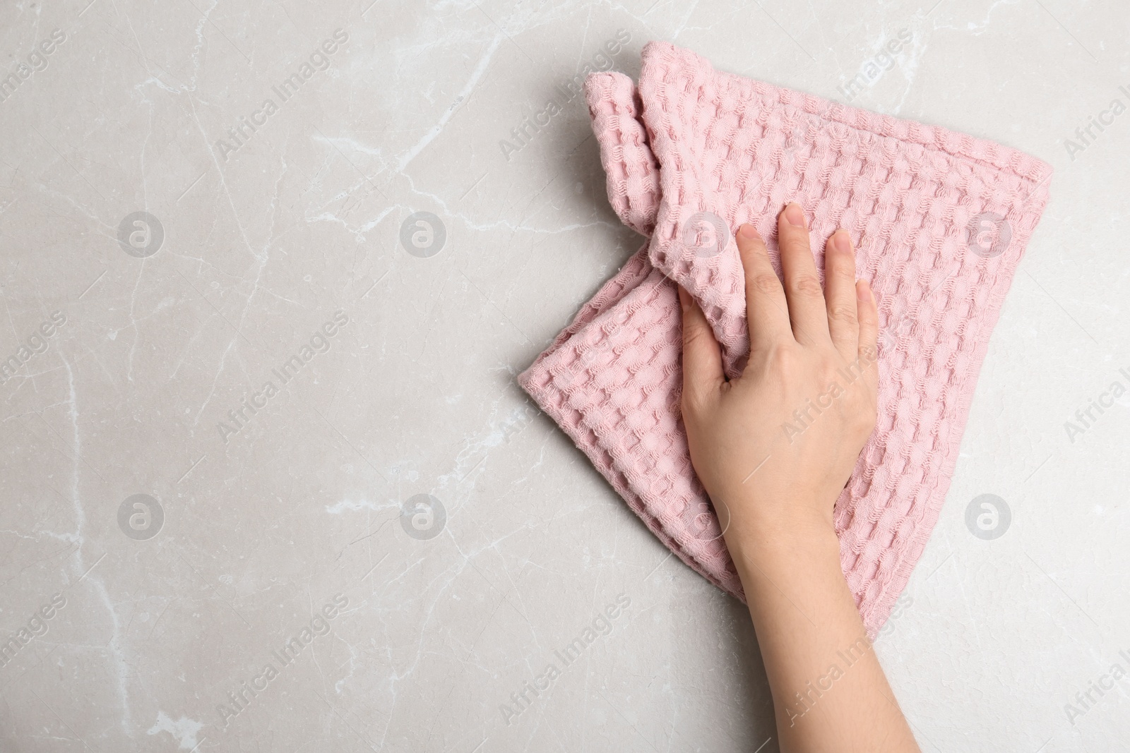 Photo of Woman wiping light grey marble table with kitchen towel, top view. Space for text