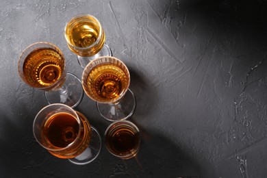 Photo of Many different liqueurs in glasses on dark textured table, flat lay. Space for text