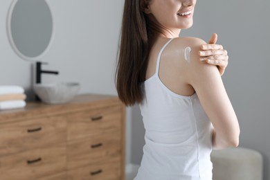 Woman applying body cream onto shoulder in bathroom, closeup. Space for text