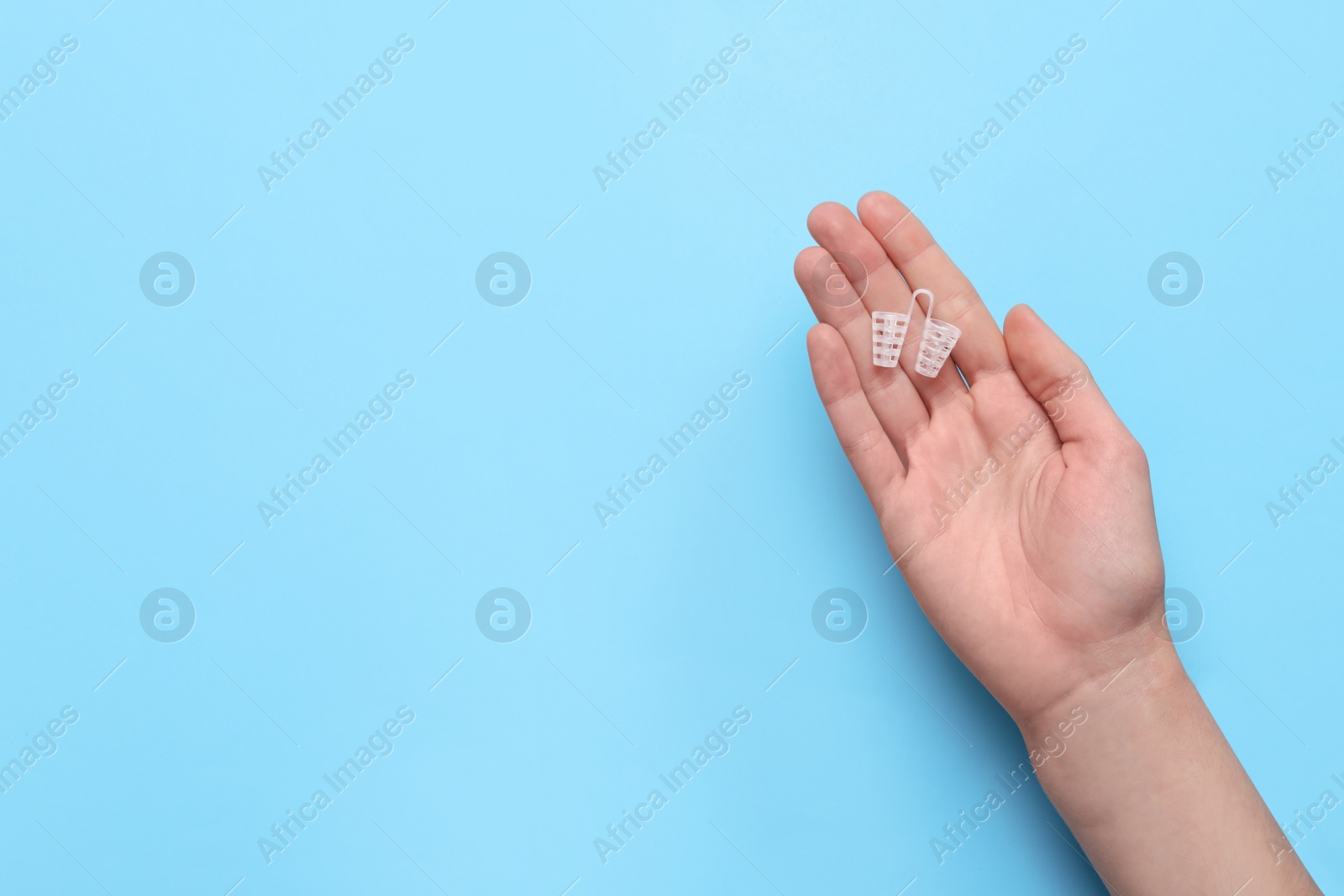 Photo of Woman holding anti-snoring device on light blue background, top view. Space for text