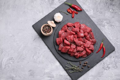 Photo of Pieces of raw beef meat, products and spices on grey textured table, top view. Space for text