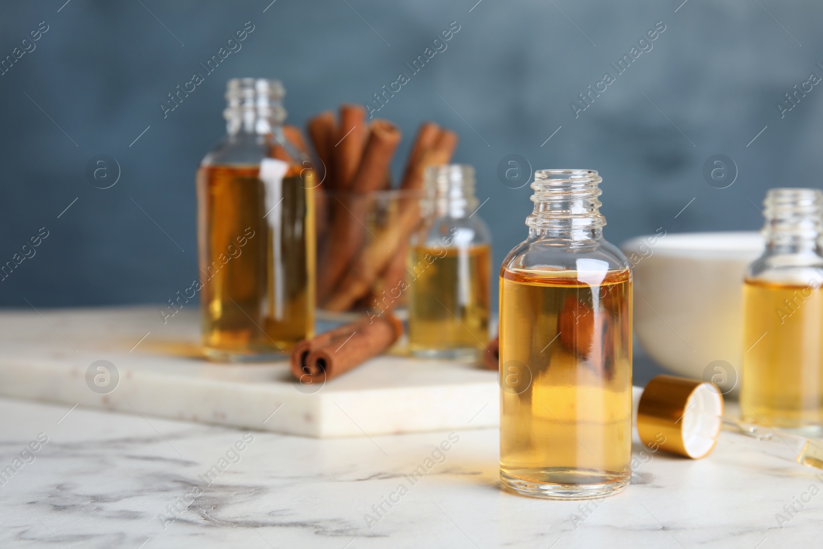 Photo of Bottles with cinnamon essential oil on marble table against blue background. Space for text