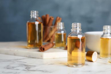 Photo of Bottles with cinnamon essential oil on marble table against blue background. Space for text