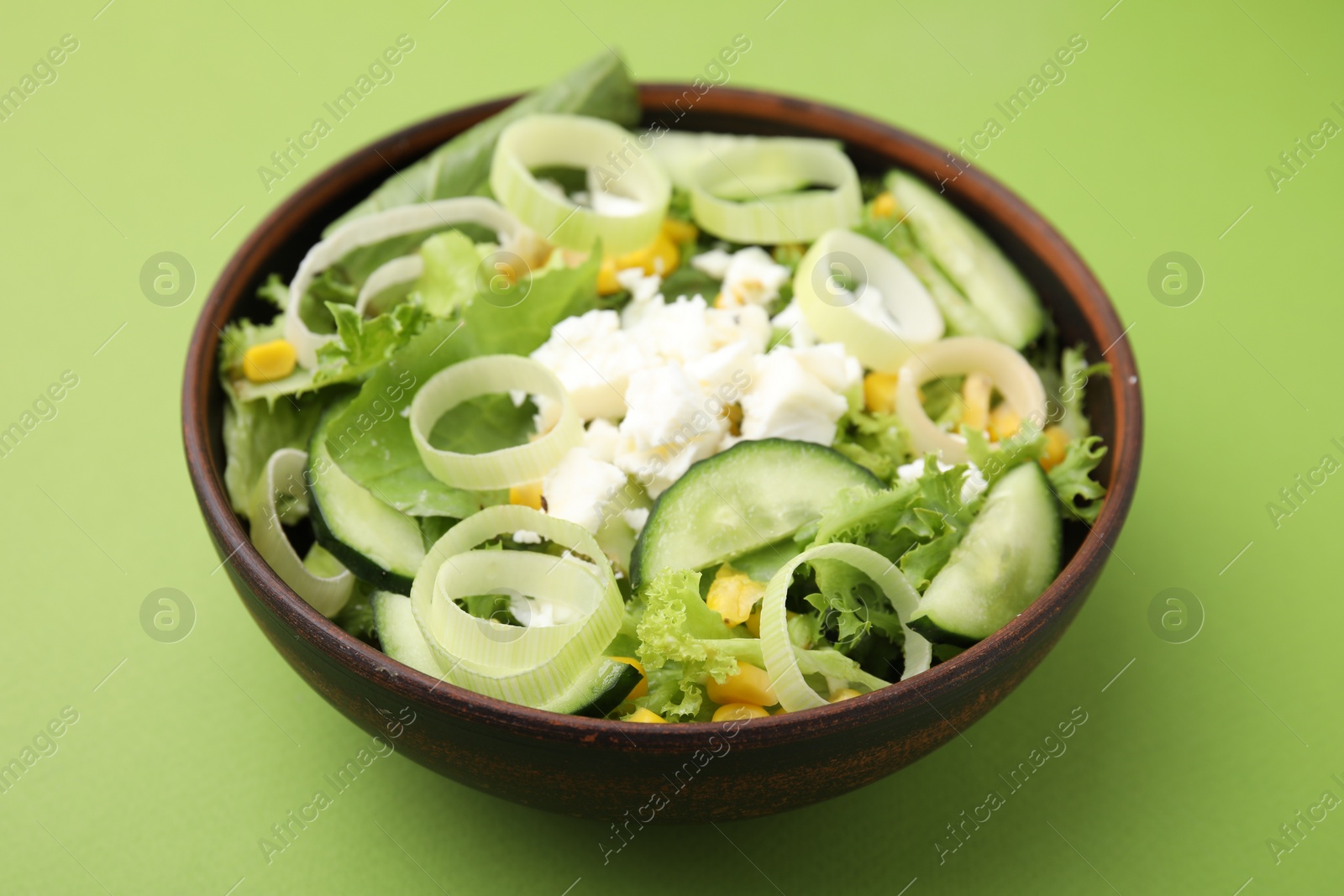 Photo of Bowl of tasty salad with leek and cheese on green table, closeup