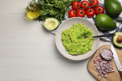 Delicious guacamole in bowl and ingredients on white wooden table, flat lay. Space for text