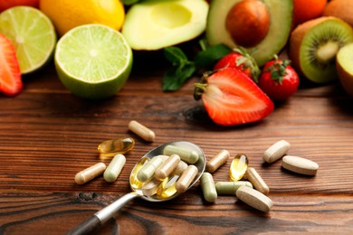 Different vitamin pills and fresh fruits on wooden table