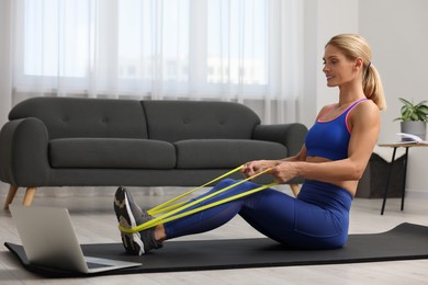 Photo of Athletic woman doing exercise with fitness elastic band on mat at home