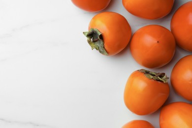 Photo of Delicious ripe persimmons on white marble table, flat lay. Space for text