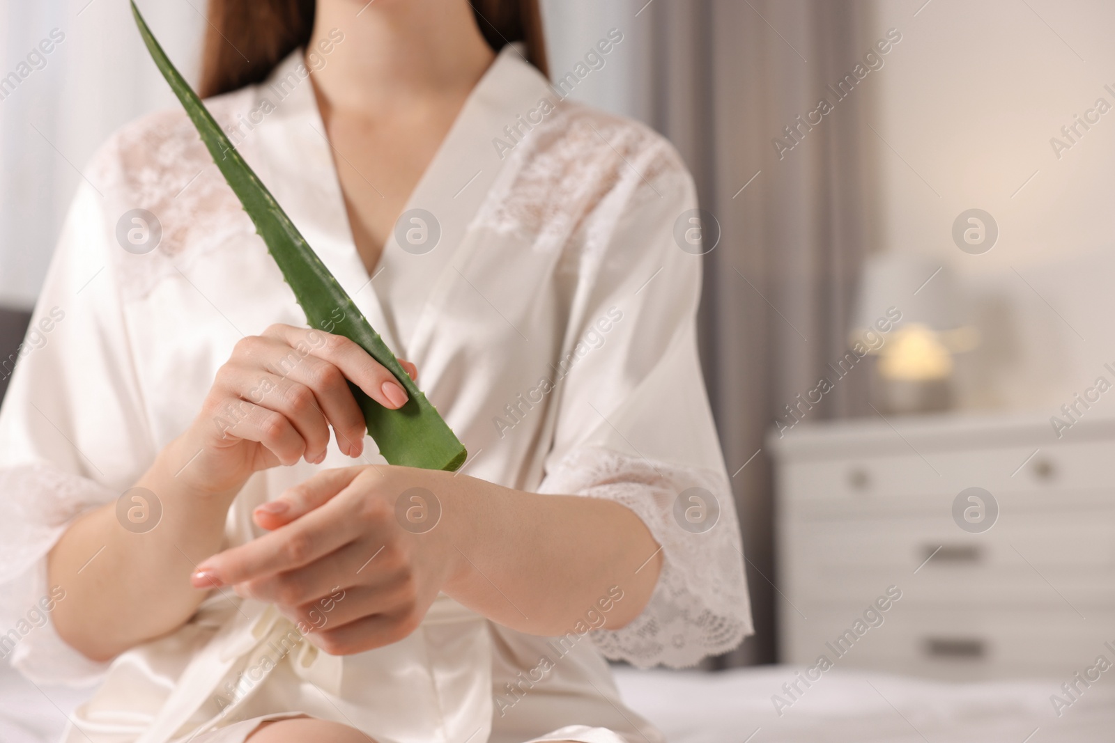 Photo of Young woman applying aloe gel from leaf onto her arm indoors, closeup. Space for text