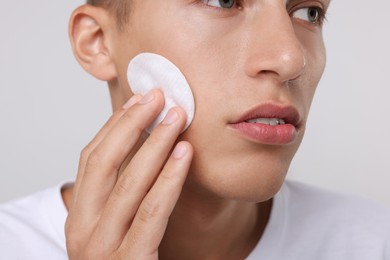 Photo of Man cleaning face with cotton pad on light background, closeup