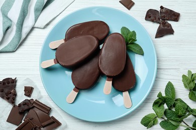 Flat lay composition with glazed ice cream bars, fresh mint and chocolate on white wooden table