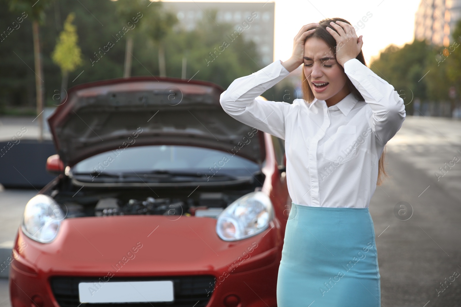 Photo of Stressed woman standing near broken car on city street