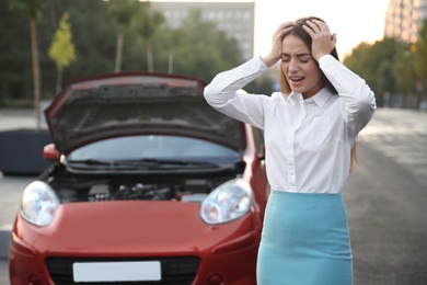 Stressed woman standing near broken car on city street