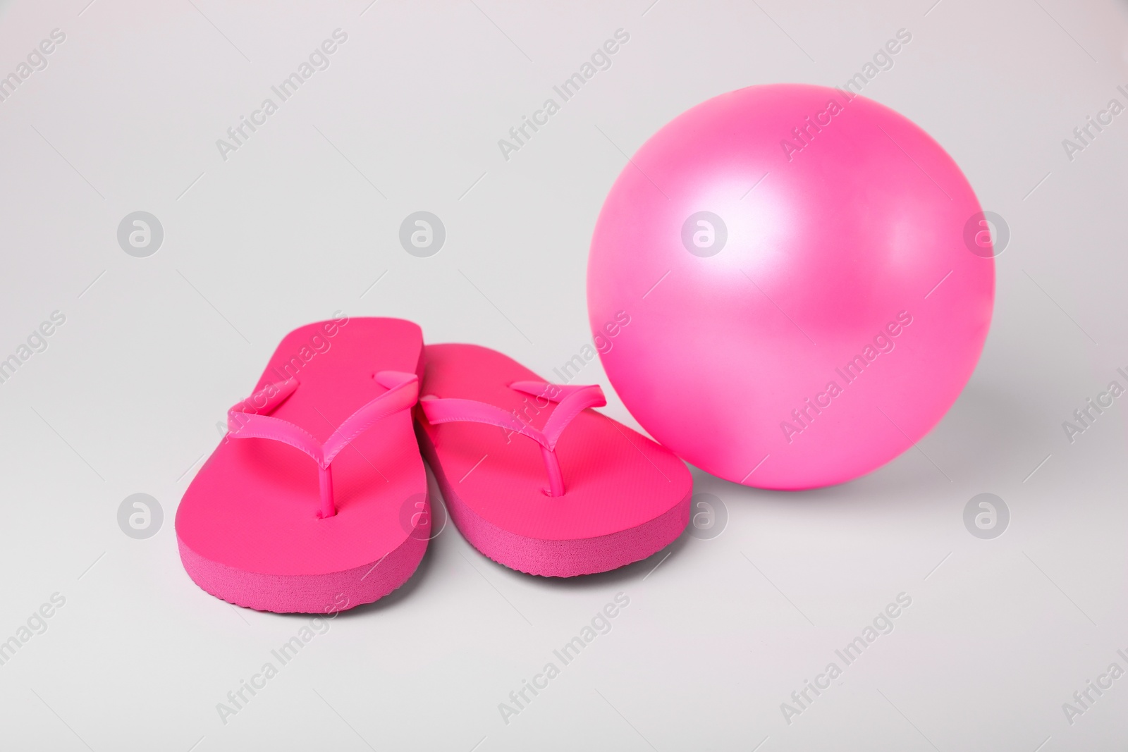 Photo of Pink inflatable beach ball and flip flops on white background