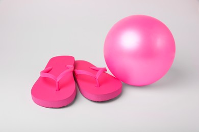 Photo of Pink inflatable beach ball and flip flops on white background